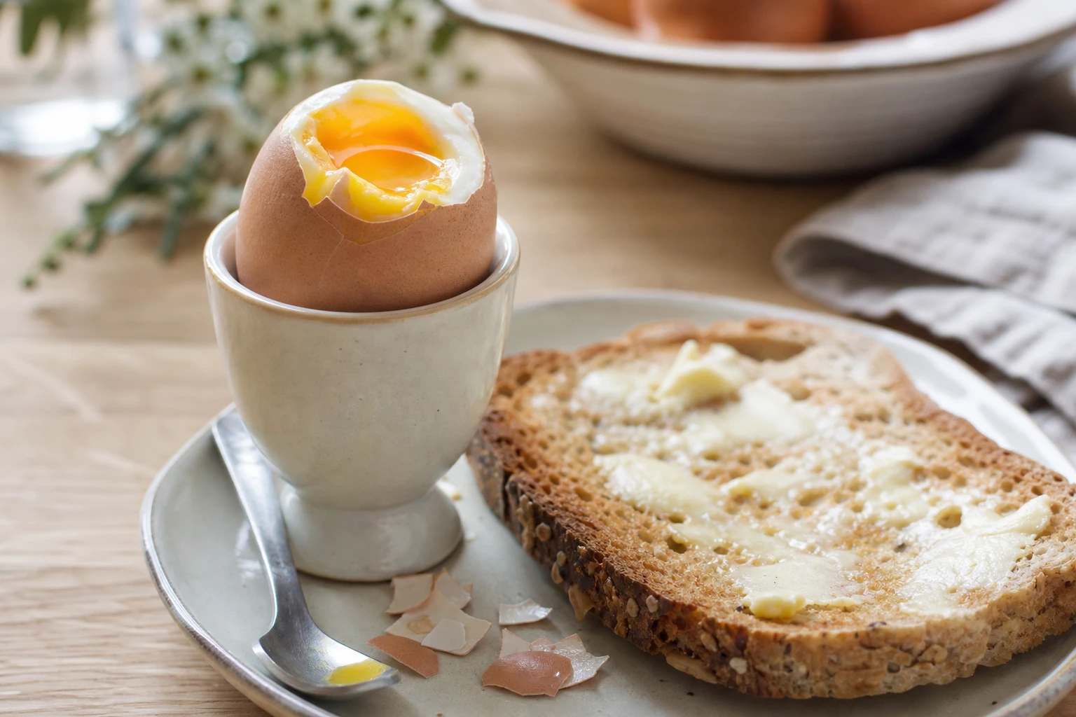 Œuf à la coque dans son coquetier à côté d'une tartine de pain complet beurrée, petit-déjeuner protéiné pour enfant